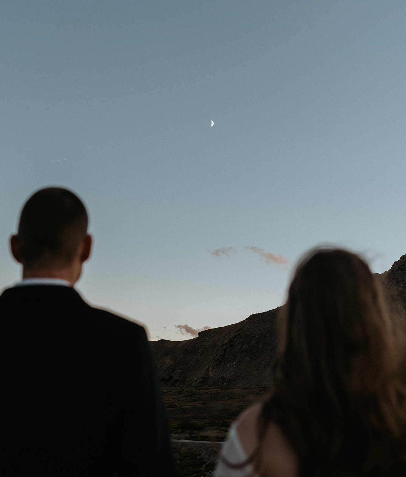 Newlyweds hold hands while looking at the moon above the mountains on their Colorado Adventure Elopement