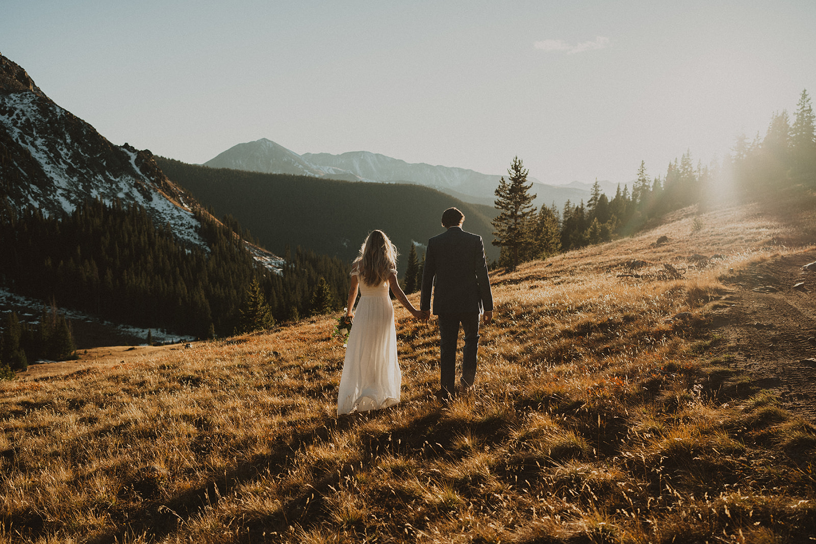 Newlyweds walk away into the sunset on a remote mountain hillside during their Colorado Helicopter Wedding