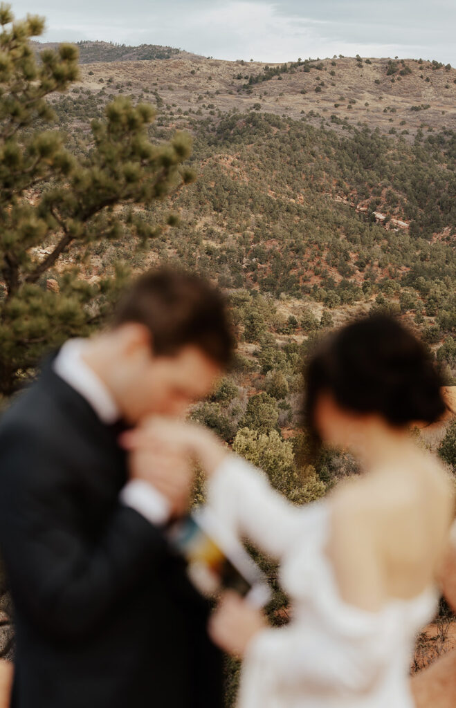 Out of focus photo of a groom kissing his brides hands as they exchange their vows in Colorado