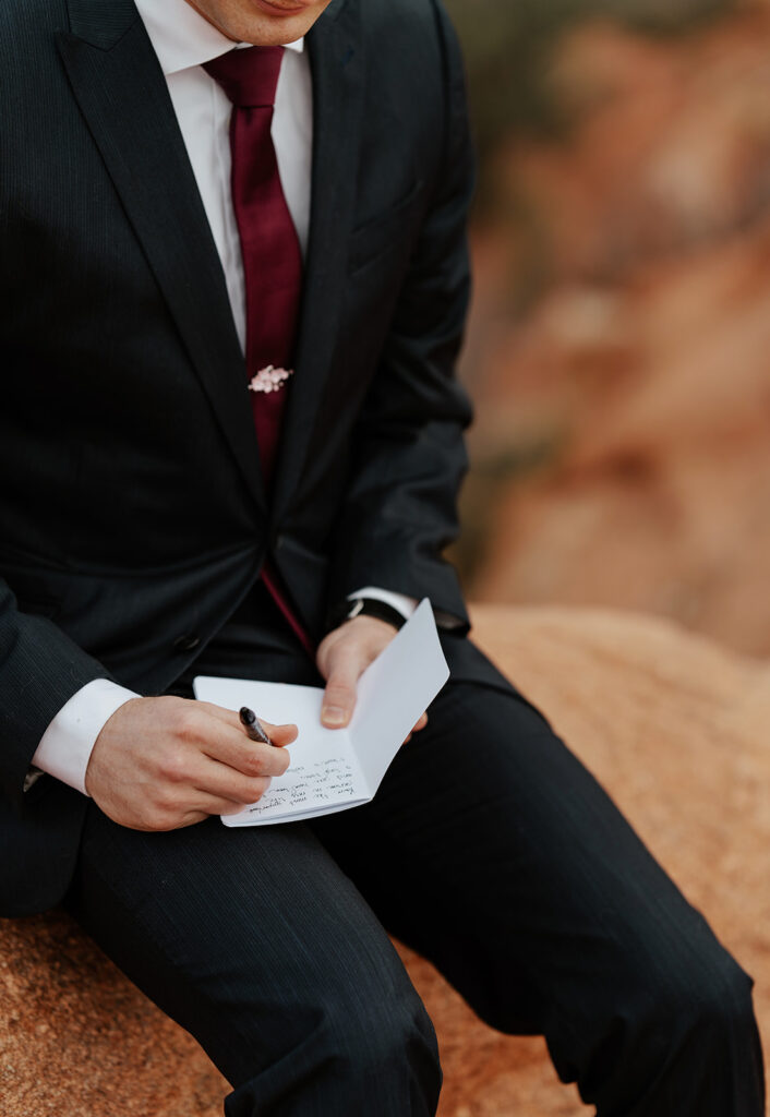 Close up photo of a groom sitting on a rock as he writes his personal vows