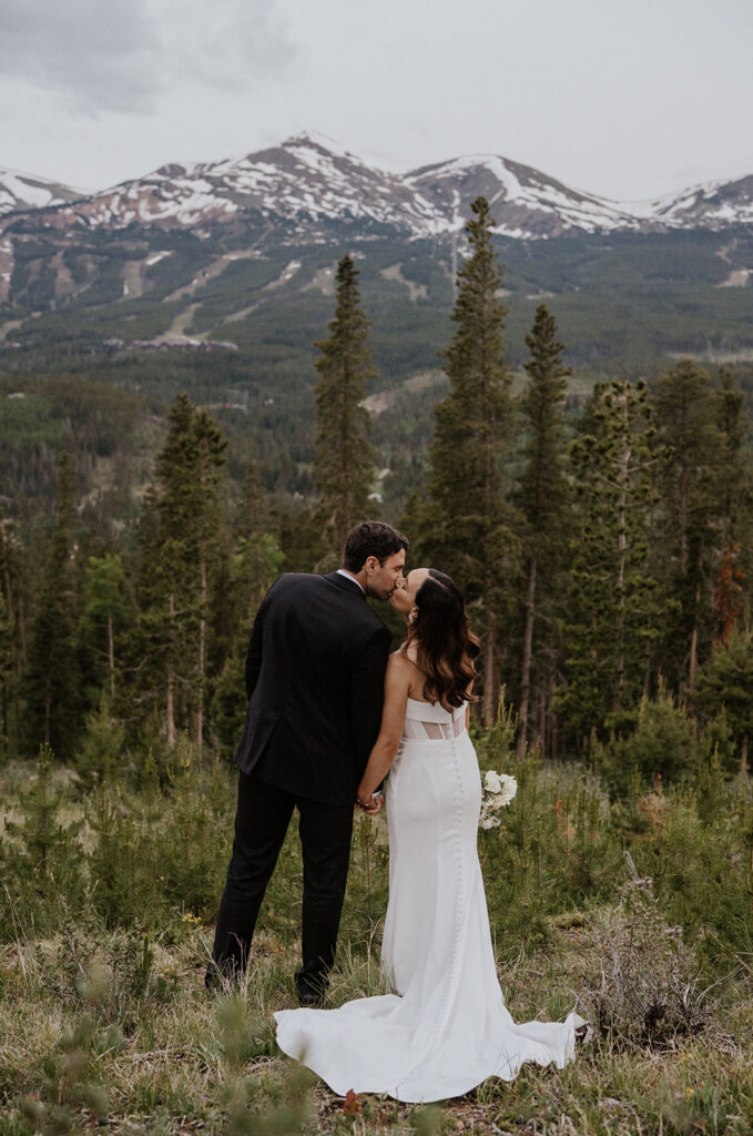 Bride and groom kissing with mountain backdrops during their Airbnb elopement in Breckenridge, Colorado at Northwoods