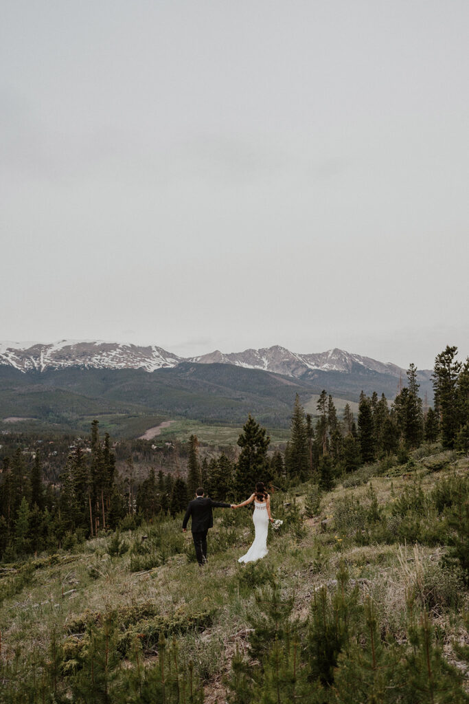 Bride and groom holding hands and walking with mountain backdrops during their Airbnb elopement in Breckenridge, Colorado at Northwoods