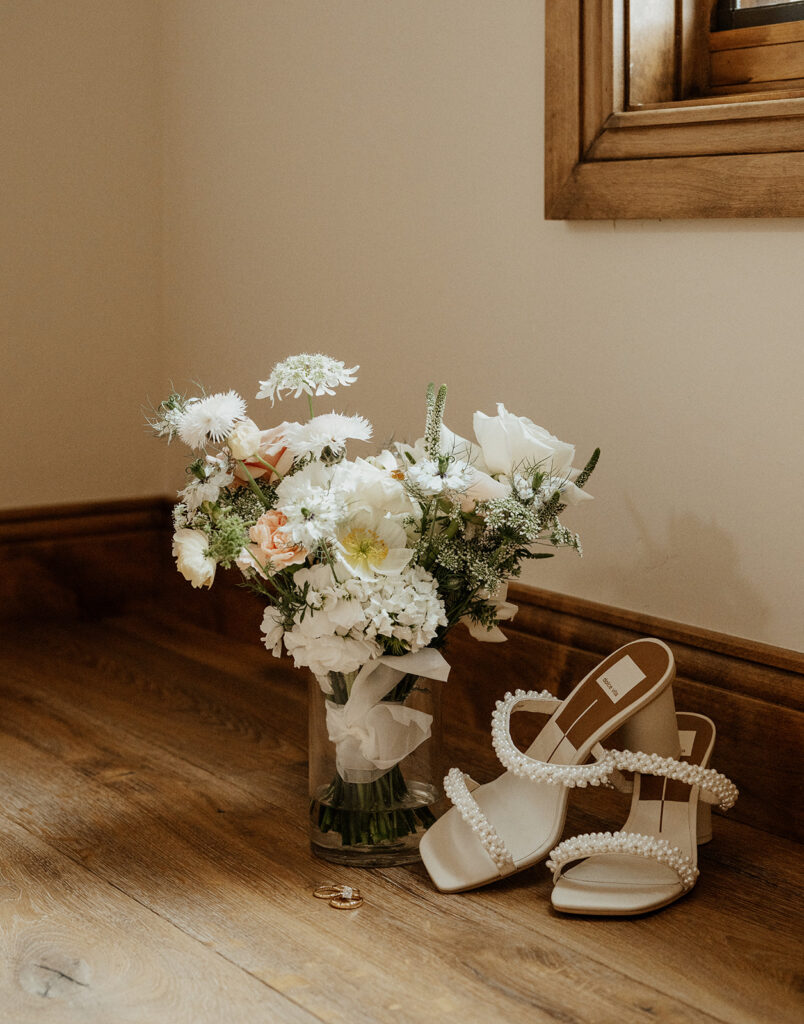 Brides heels, wedding bouquet, and rings sitting on the floor as she gets ready for her Airbnb elopement in Breckenridge, Colorado at Northwoods