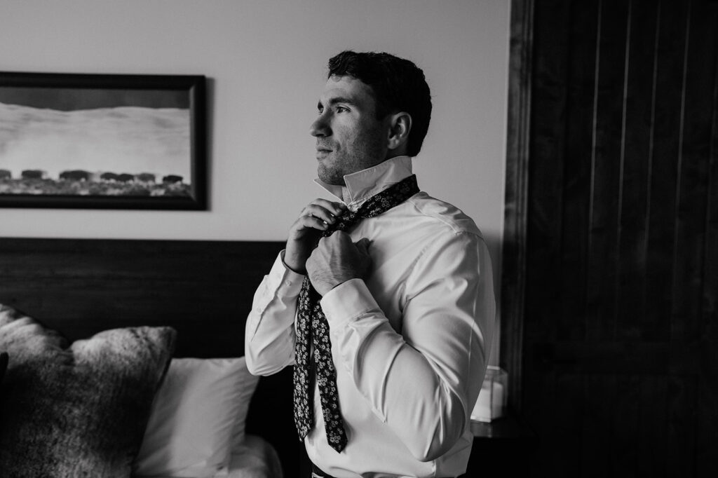 Black and white photo of a groom getting ready for his Airbnb elopement in Breckenridge, Colorado at Northwoods