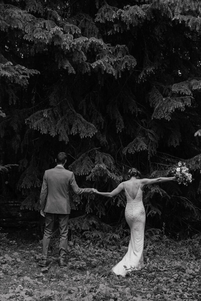 Black and white photo of a bride and groom holding hands in the woods