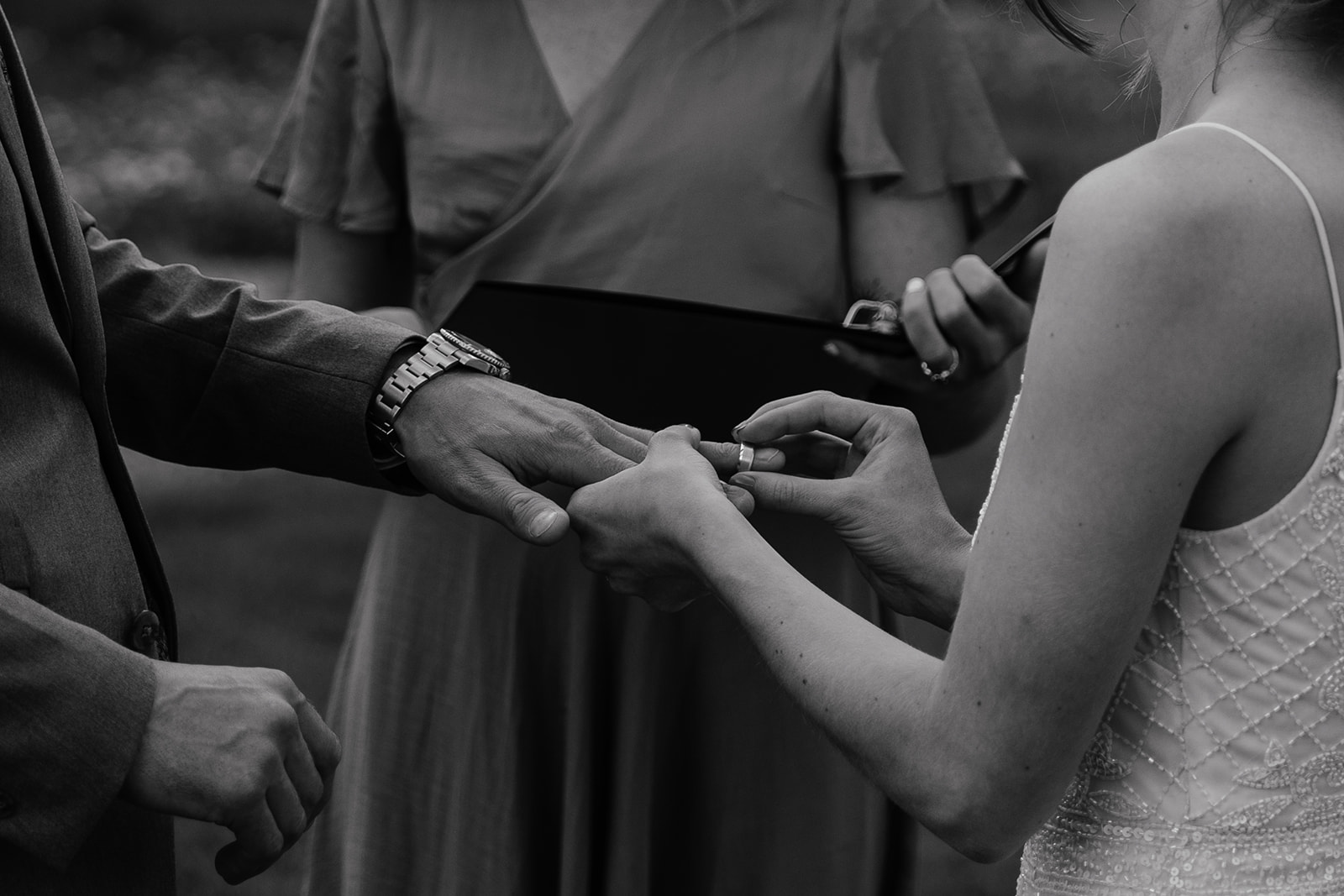 Black and white photo of a bride putting the band on her grooms finger