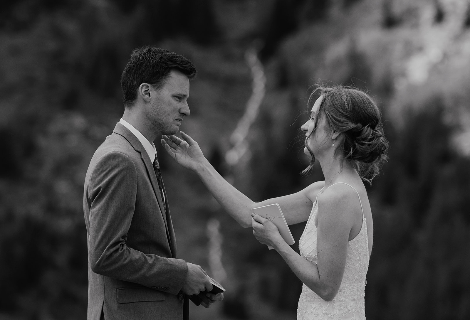 Black and white photo of a bride wiping grooms tears away during their emotional private vow exchange for their Colorado mountain elopement