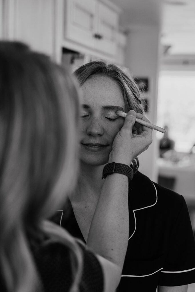 Black and white photo of a bride getting her makeup done by Olivine Hair Studio