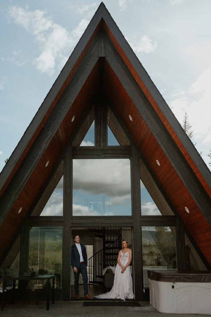 Bride and groom posing for portraits outside of their a-frame cabin during their Alaska elopement