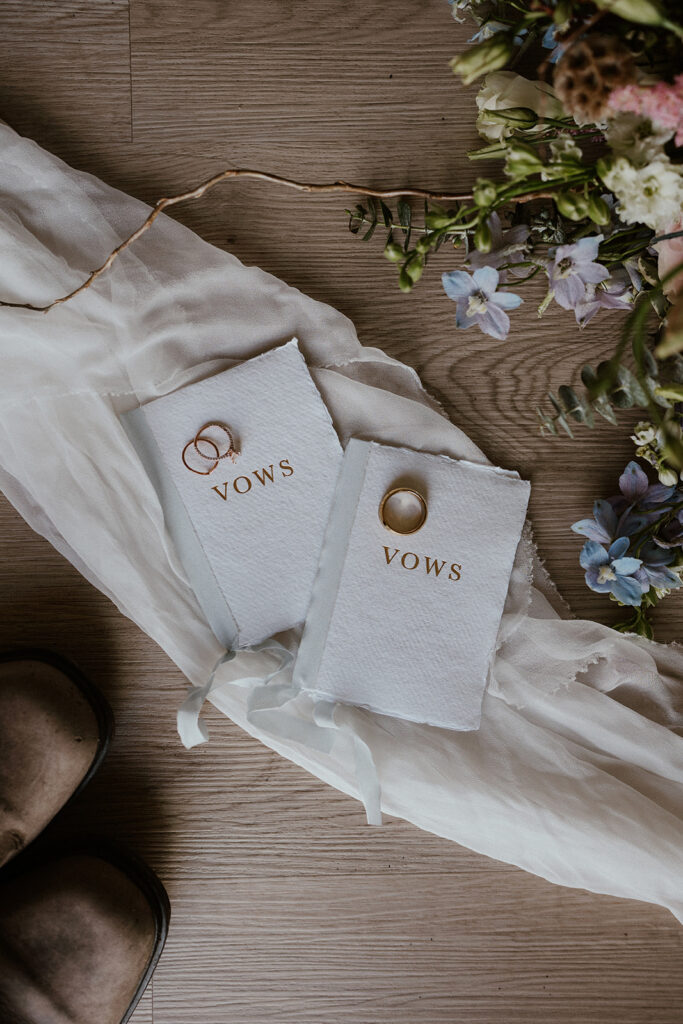 Bride and grooms white foil vow books, wedding rings, and bouquet for an elopement detail shot