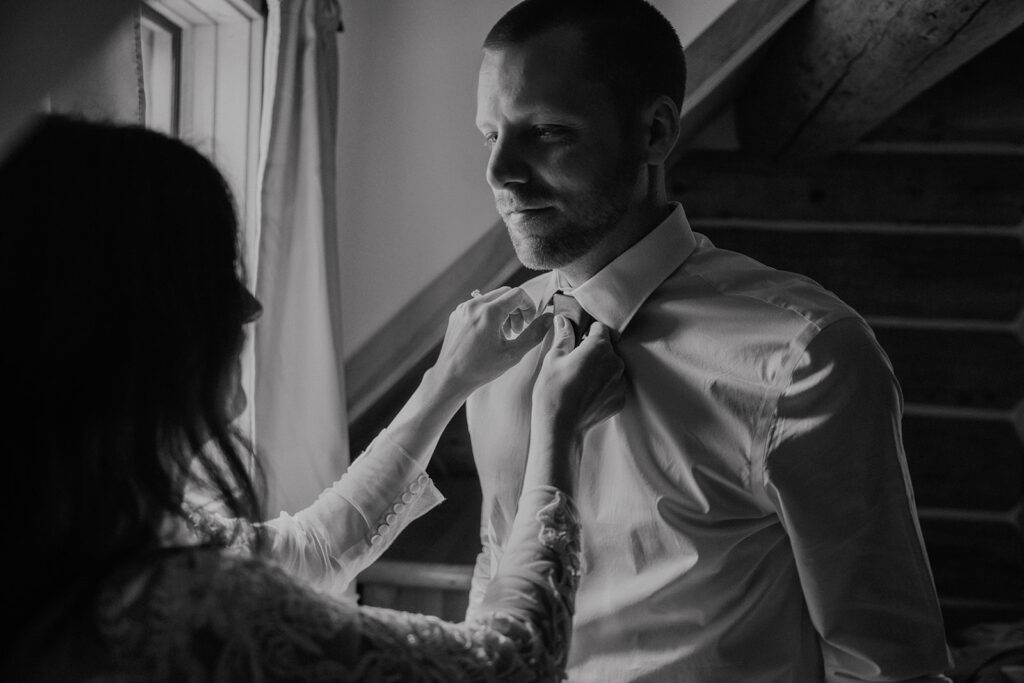 Black and white photo of a bride helping her groom get ready