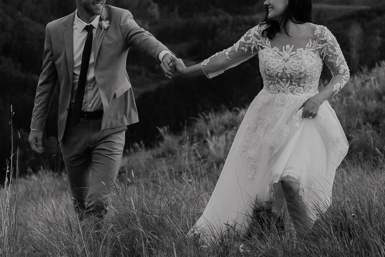 Black and white photo of a bride and groom walking through the Colorado mountains