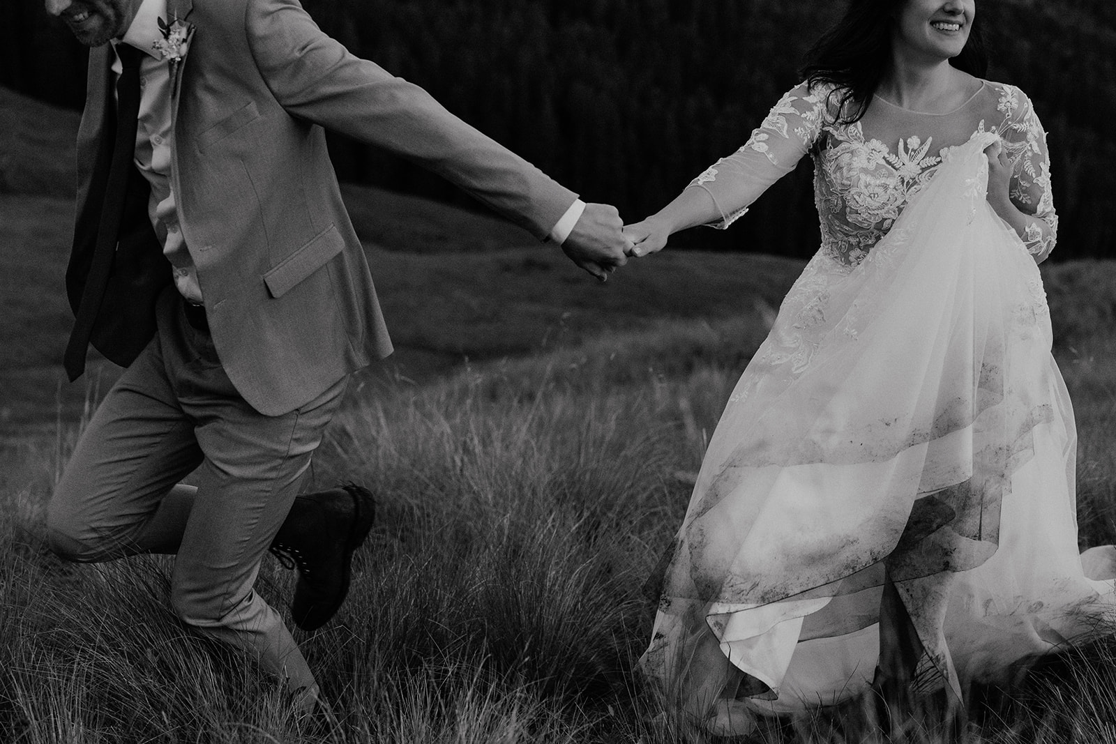 Black and white photo of a bride and groom running in the mountains