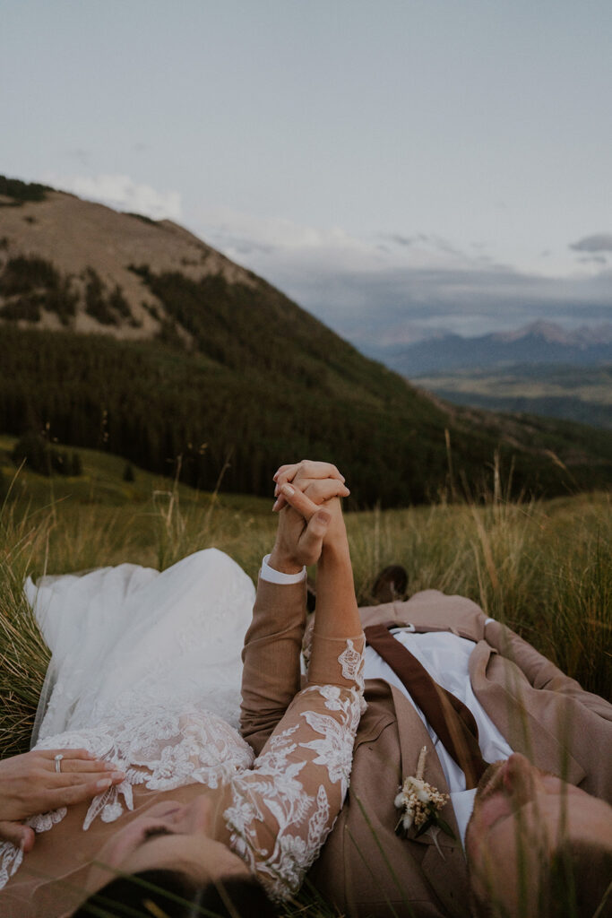 Bride and groom holding hands while they lay in the Colorado mountains