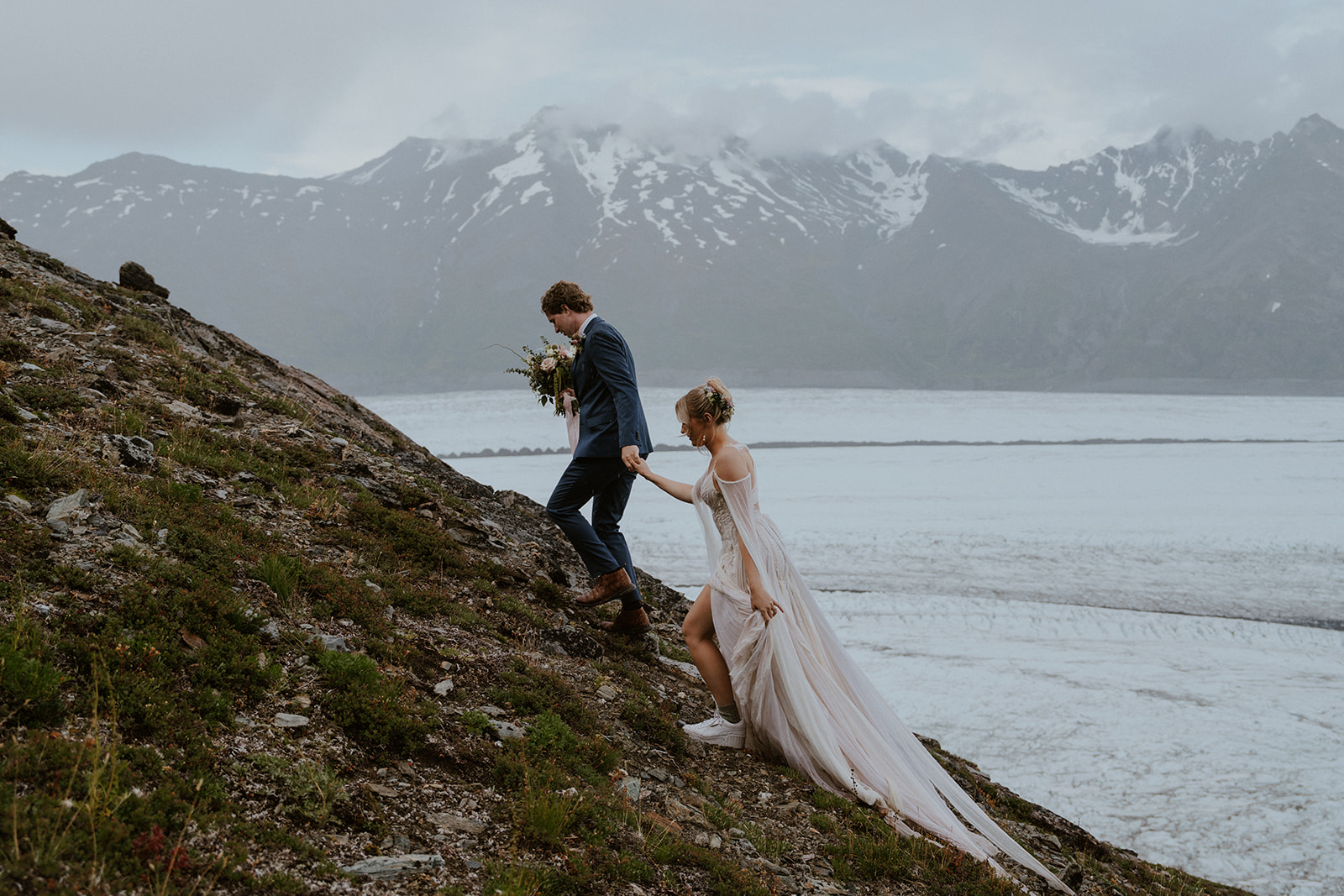 Bride and groom walking up a hill during their Knik Glacier elopement in Alaska