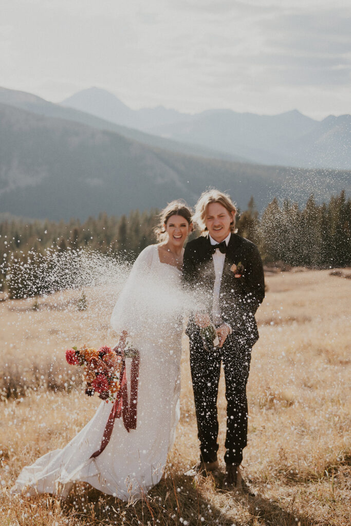 Bride and groom popping champagne in the mountains