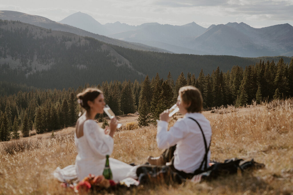 Bride and groom sipping champagne during their elopement picnic in the mountains