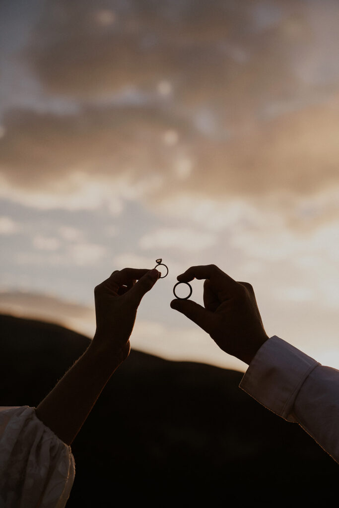 Bride and groom holding their wedding rings up to the sky during sunset