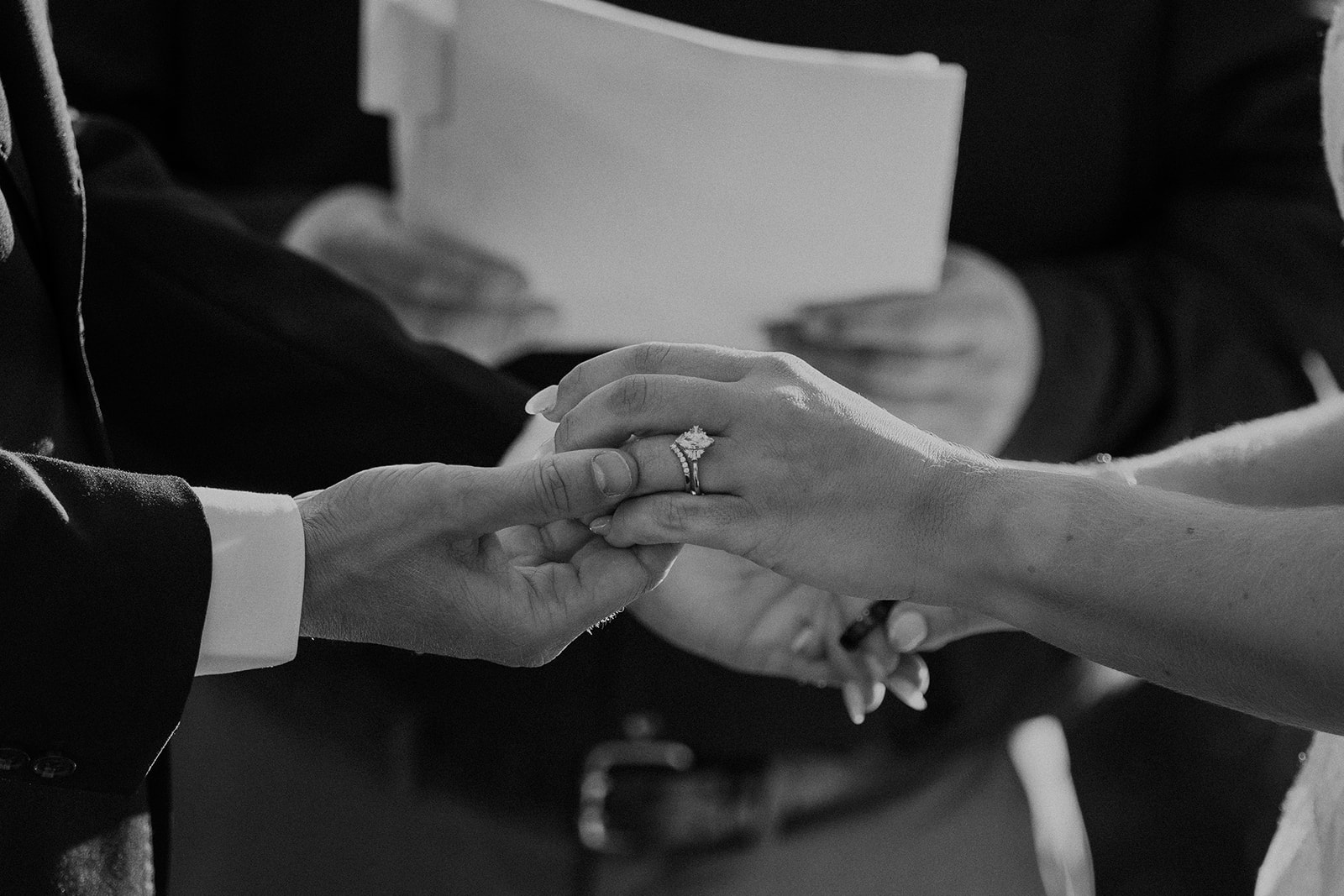 Black and white photo of a bride and groom holding hands during their ceremony