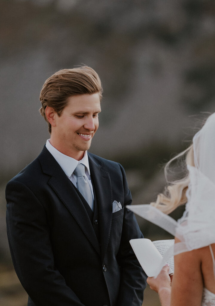 Groom smiling as the bride reads her vows to him