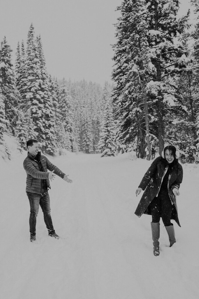 Black and white photo of a couple having a snowball fight during their snowy Colorado photoshoot